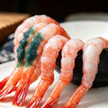 Peeled pink shrimp topped with vivid green caviar, arranged on a white plate