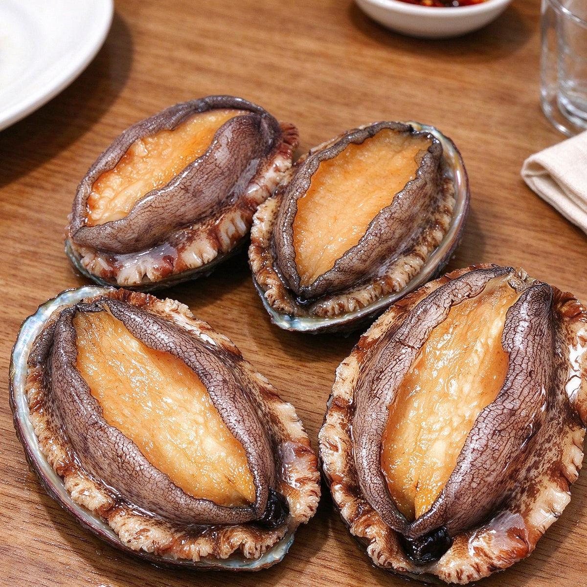 Whole abalone in dark shells with golden foot meat, resting on a steel bench
